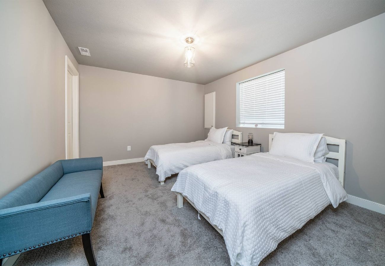 Basement bedroom featuring two twin beds with white bedding, and a blue upholstered bench.