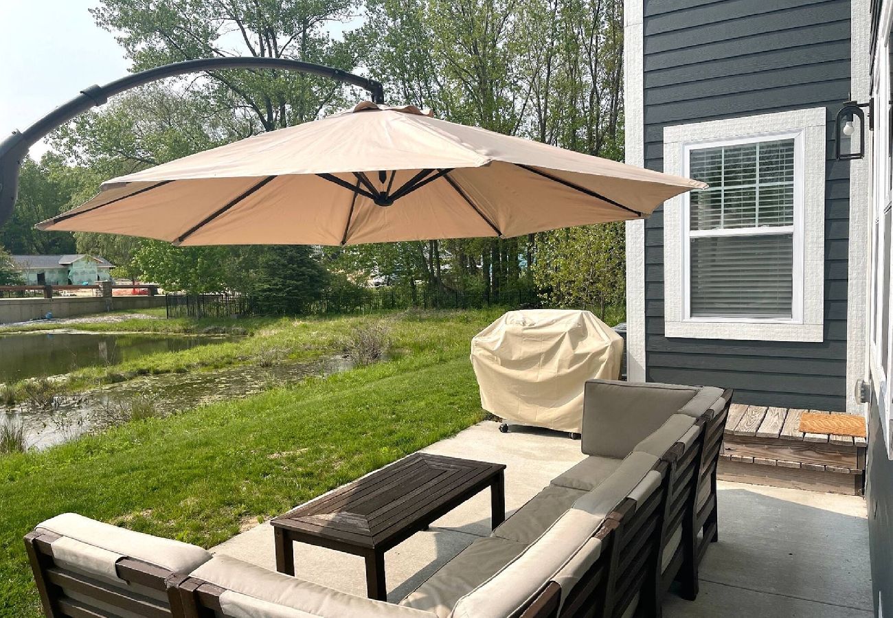 Outdoor Patio with a sectional sofa, large umbrella, grill, and a view of the grassy yard and pond behind the home