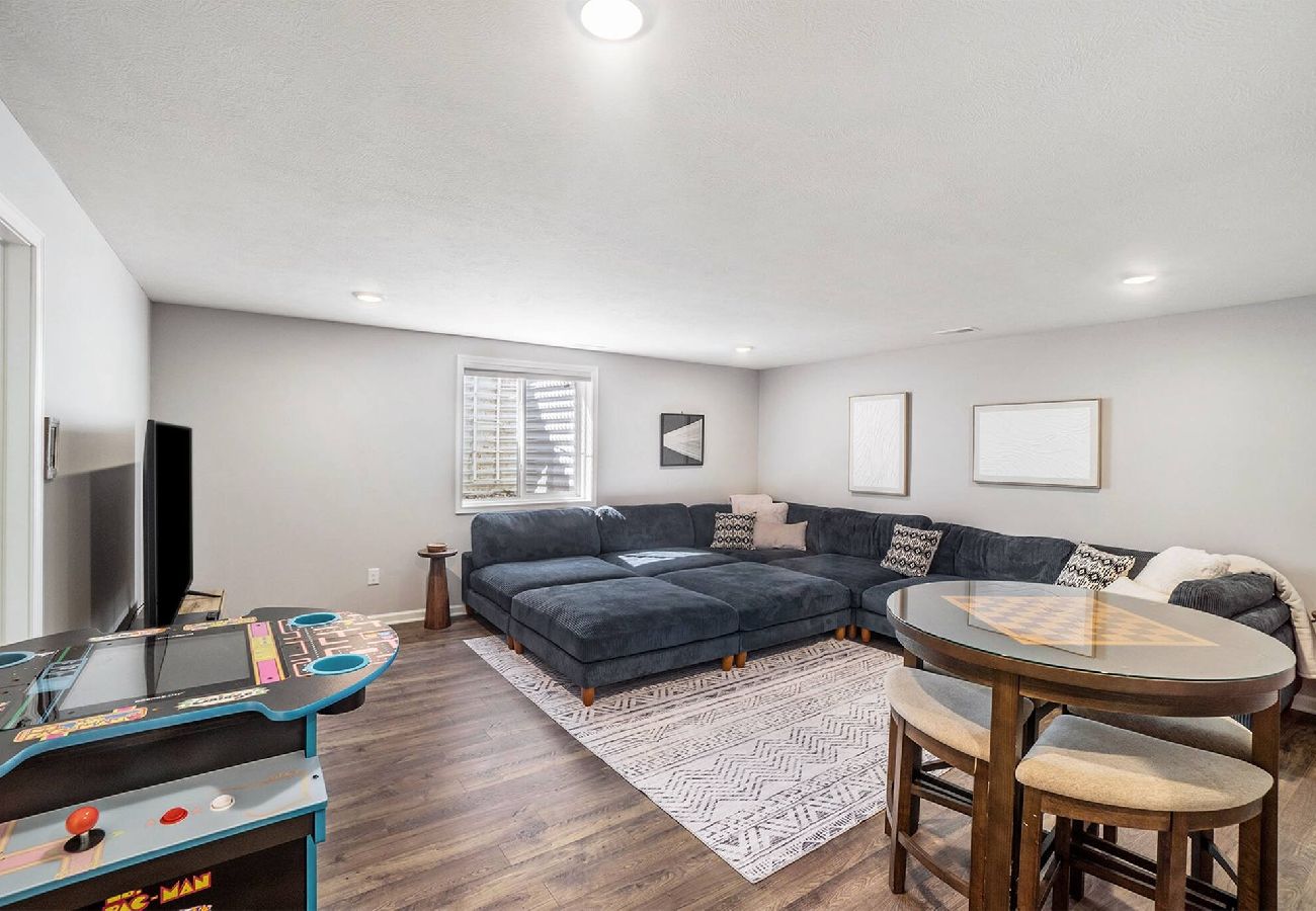 Basement living space with large sectional sofa, TV, arcade game, and game table