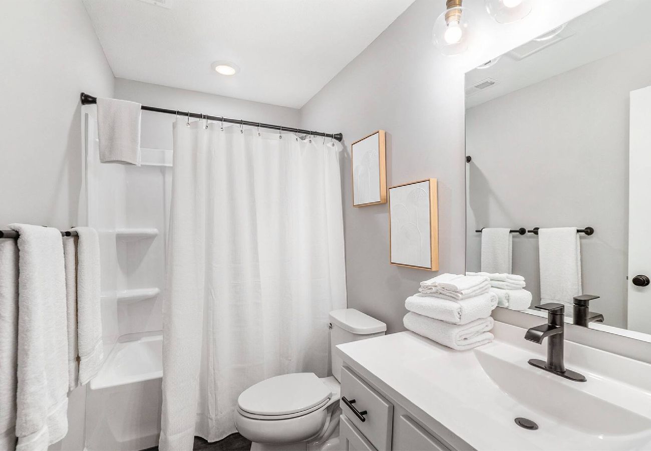 Bright bathroom with white shower, stacked towels, and black fixtures