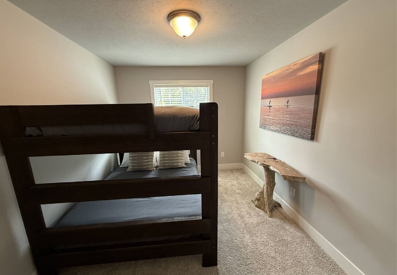 Bedroom with queen-over-queen bunk beds, window light, and beach-themed artwork in South Haven